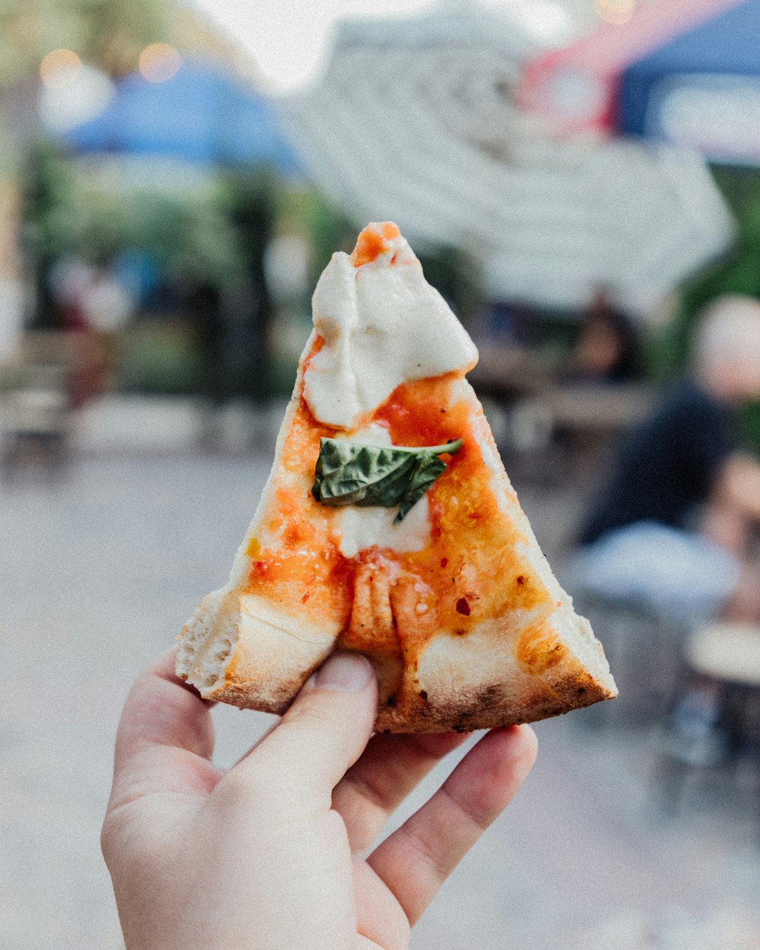 a hand holding a slice of margarita cheese pizza